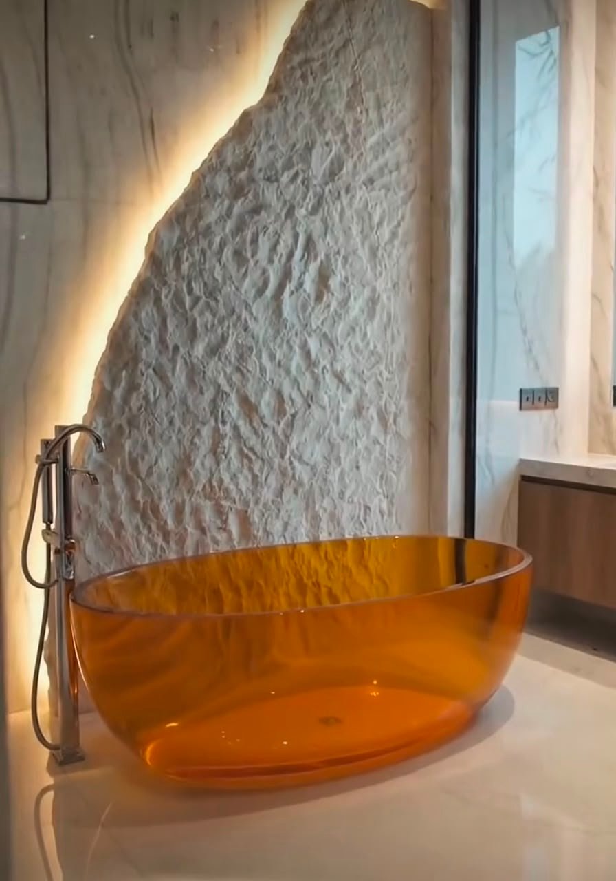 Illuminated sculpted stone slab partition behind bathtub